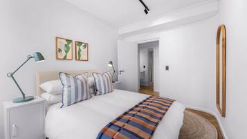Un dormitorio moderno con cama, mesitas de noche, una lámpara de escritorio y un espejo.