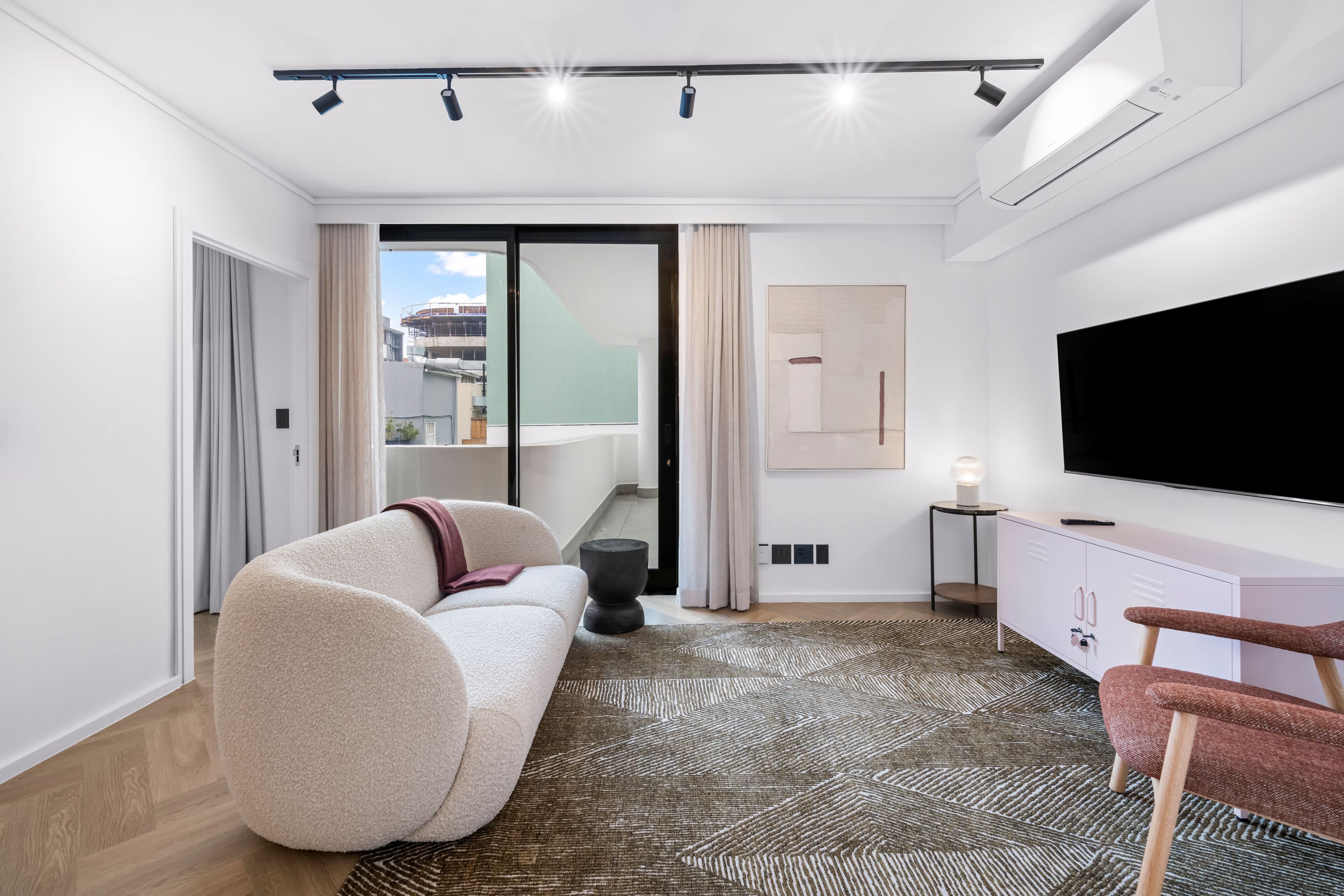 A modern living room with a sofa, a flat-screen TV, a patterned rug, and a view of the outside.
