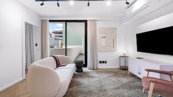 Un salon moderne avec un canapé, un téléviseur à écran plat, un tapis à motifs et une vue sur l’extérieur.