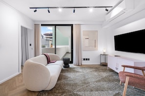 A modern living room with a sofa, a flat-screen TV, a patterned rug, and a view of the outside. - Apartments by Morea Sea Point (Cape Town)