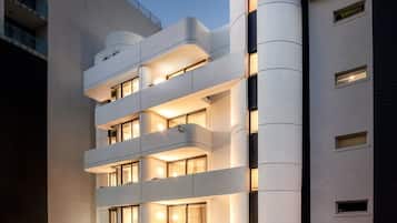 Un hôtel à plusieurs étages, doté d’un design moderne, avec des balcons à chaque niveau, une structure cylindrique imposante sur le côté droit et une entrée bien visible avec une enseigne.