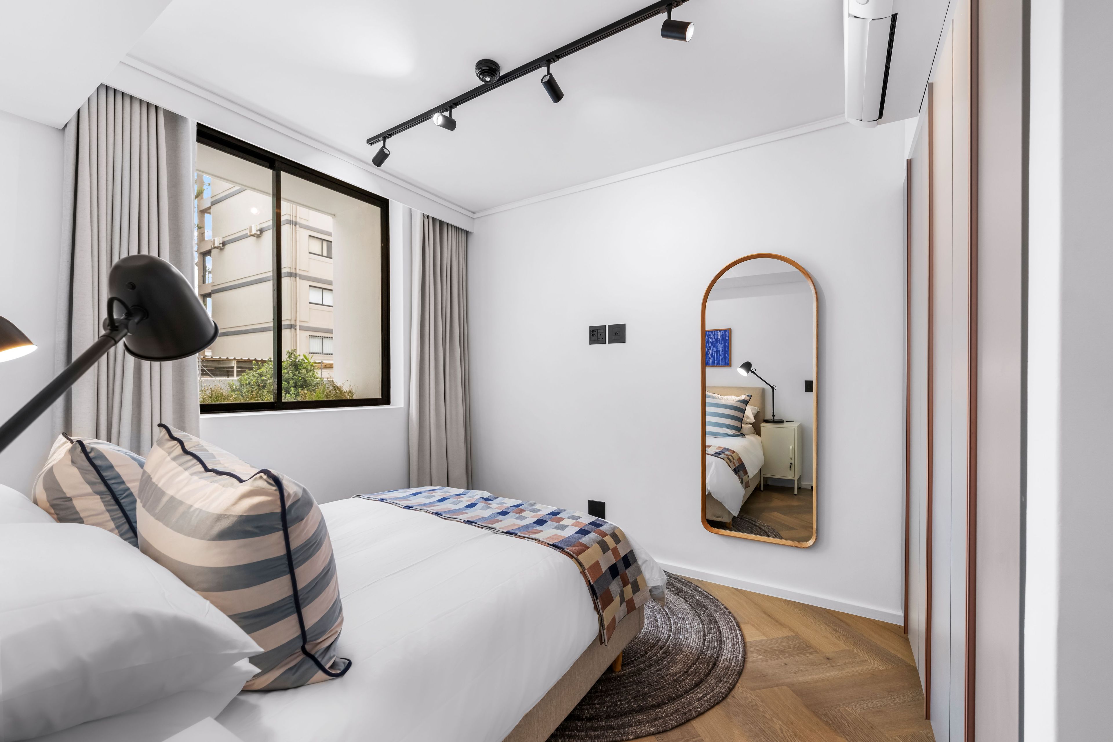 Un dormitorio moderno con una cama, una lámpara de noche, un espejo y vistas al exterior.