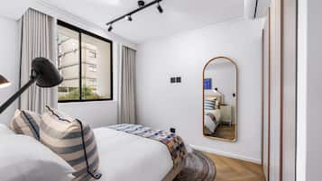 Un dormitorio moderno con una cama, una lámpara de noche, un espejo y vistas al exterior.