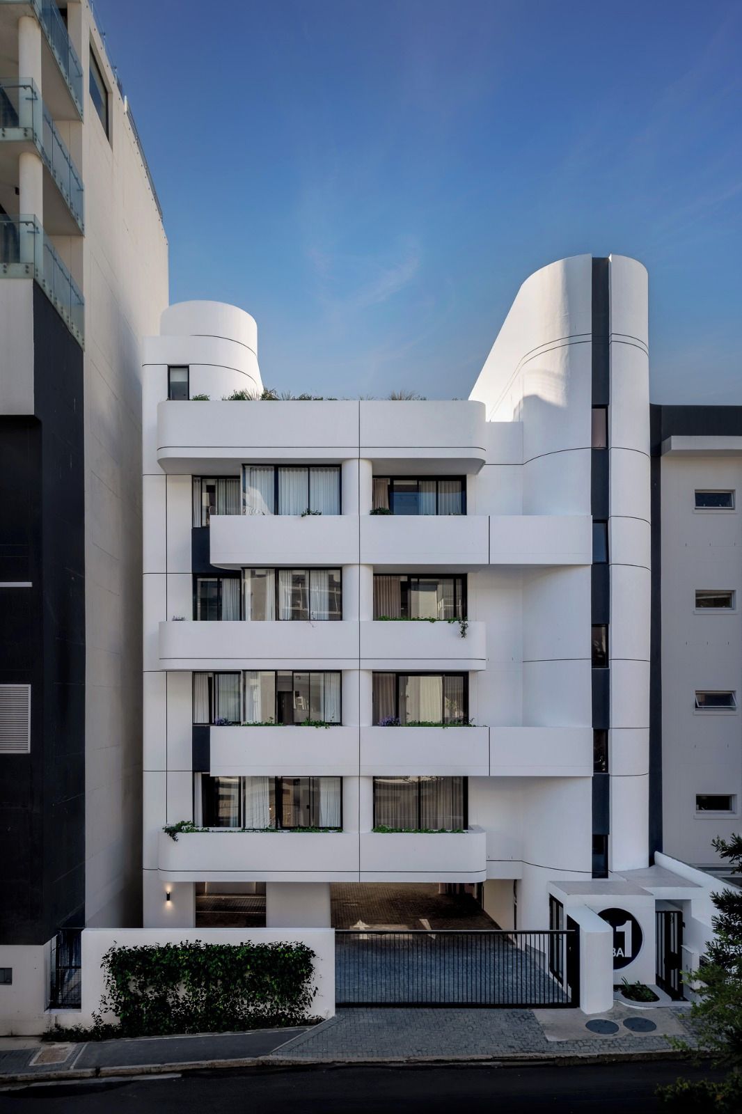 A modern building with a curved facade, multiple balconies, and a gated entrance.