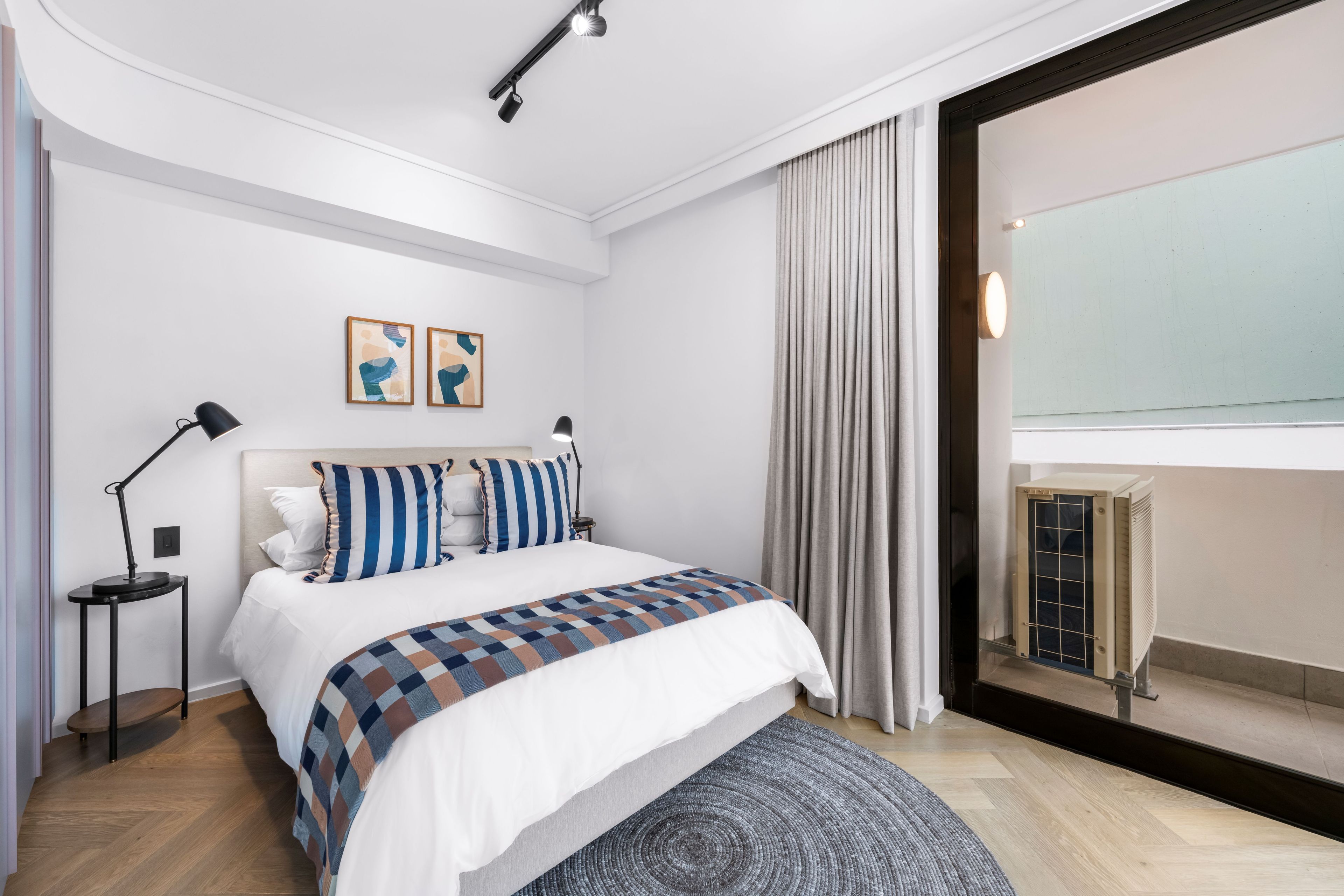 A modern hotel room with a large bed, a bedside table, a standing lamp, and a window with curtains.