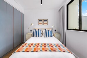 Habitación de hotel con cama, dos mesitas de noche, una ventana y vista al cielo.