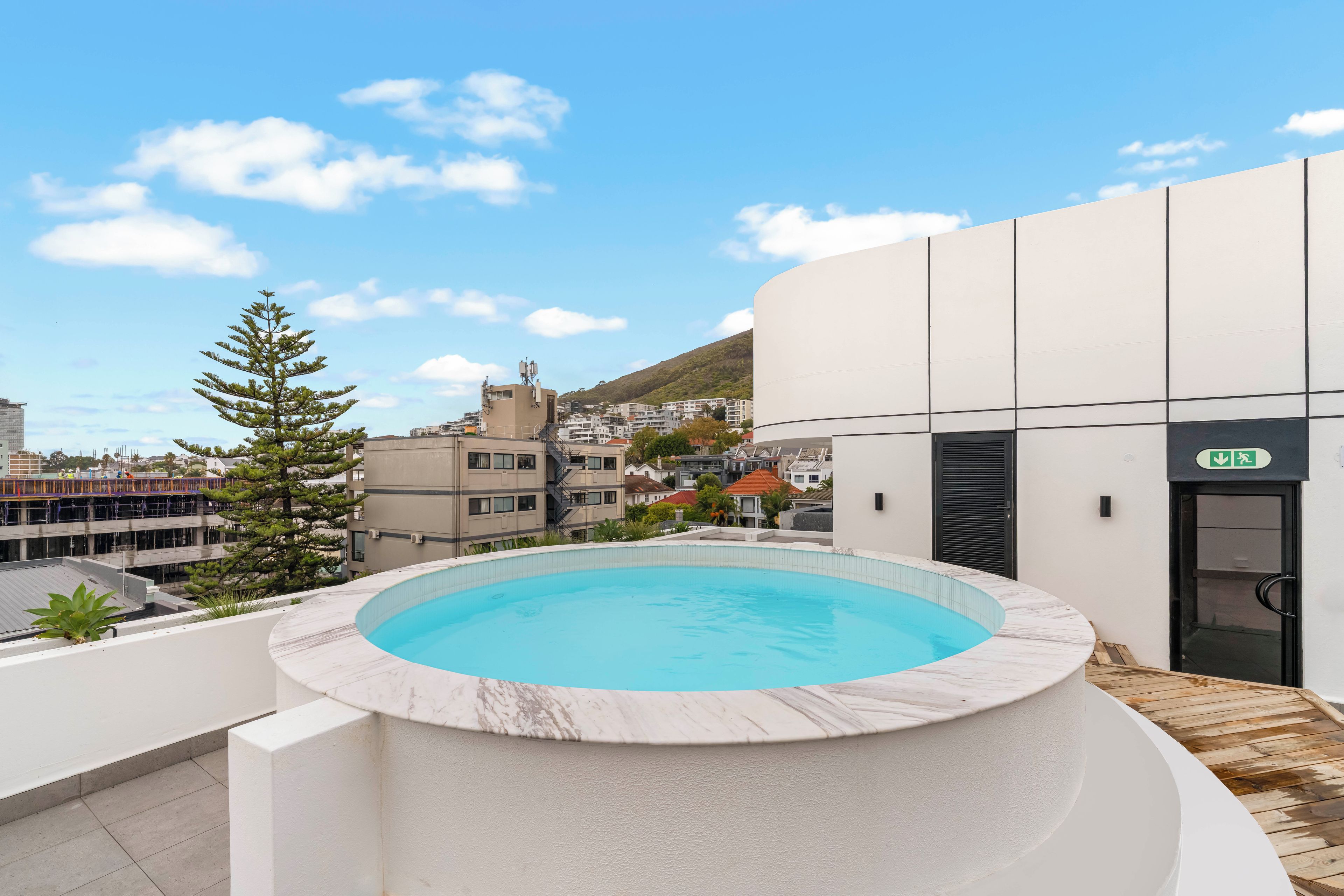 Piscina en la azotea con vistas a una zona residencial y una colina al fondo.