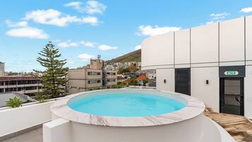 Piscina en la azotea con vistas a una zona residencial y una colina al fondo.