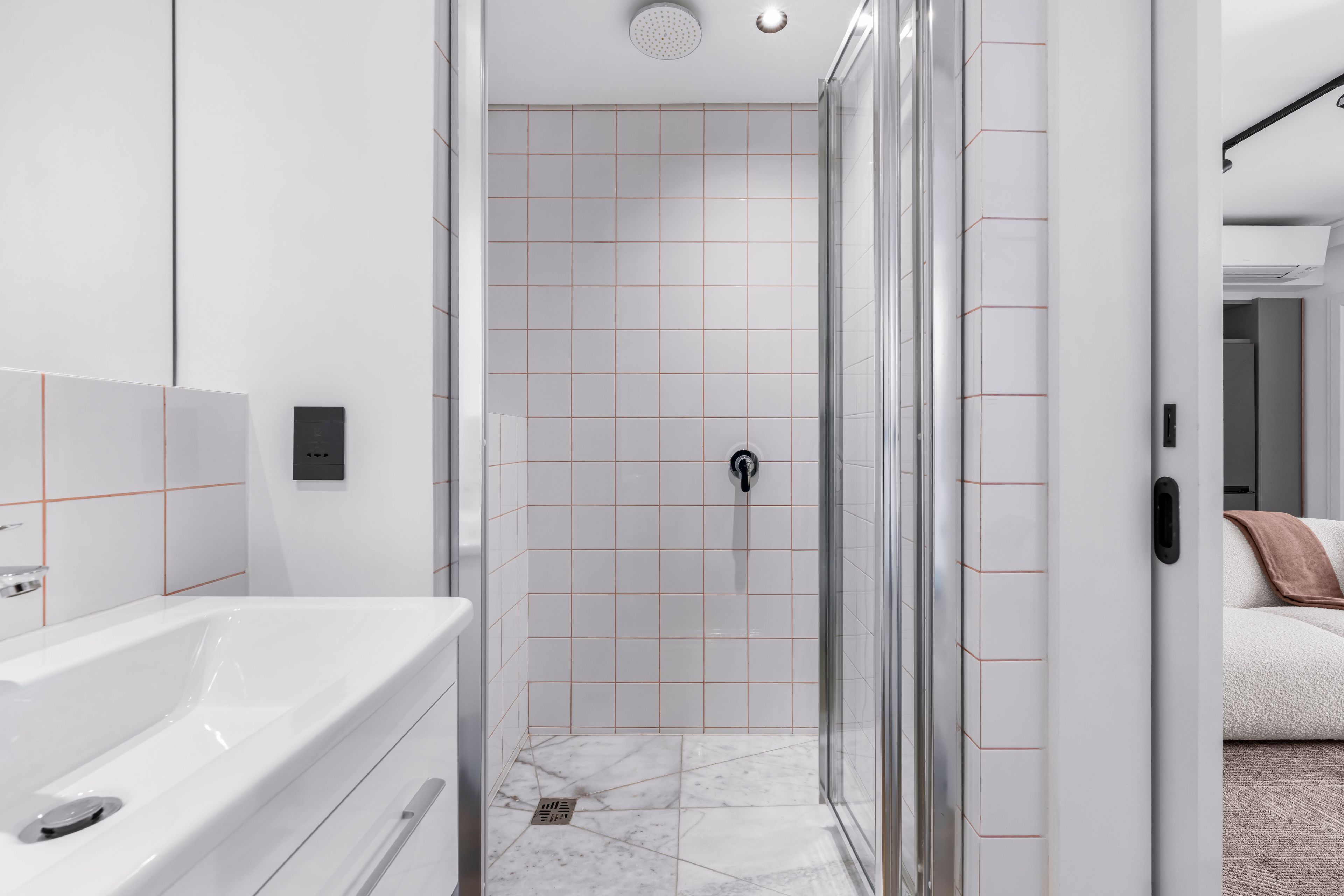 Une salle de bain moderne avec une douche à parois de verre, des carreaux blancs et un sol en marbre.