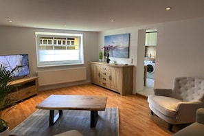 A living room with a wooden table, a sofa, a television, a window, and a kitchen area. - Holiday apartment with 1 bedroom (Insel Poel)