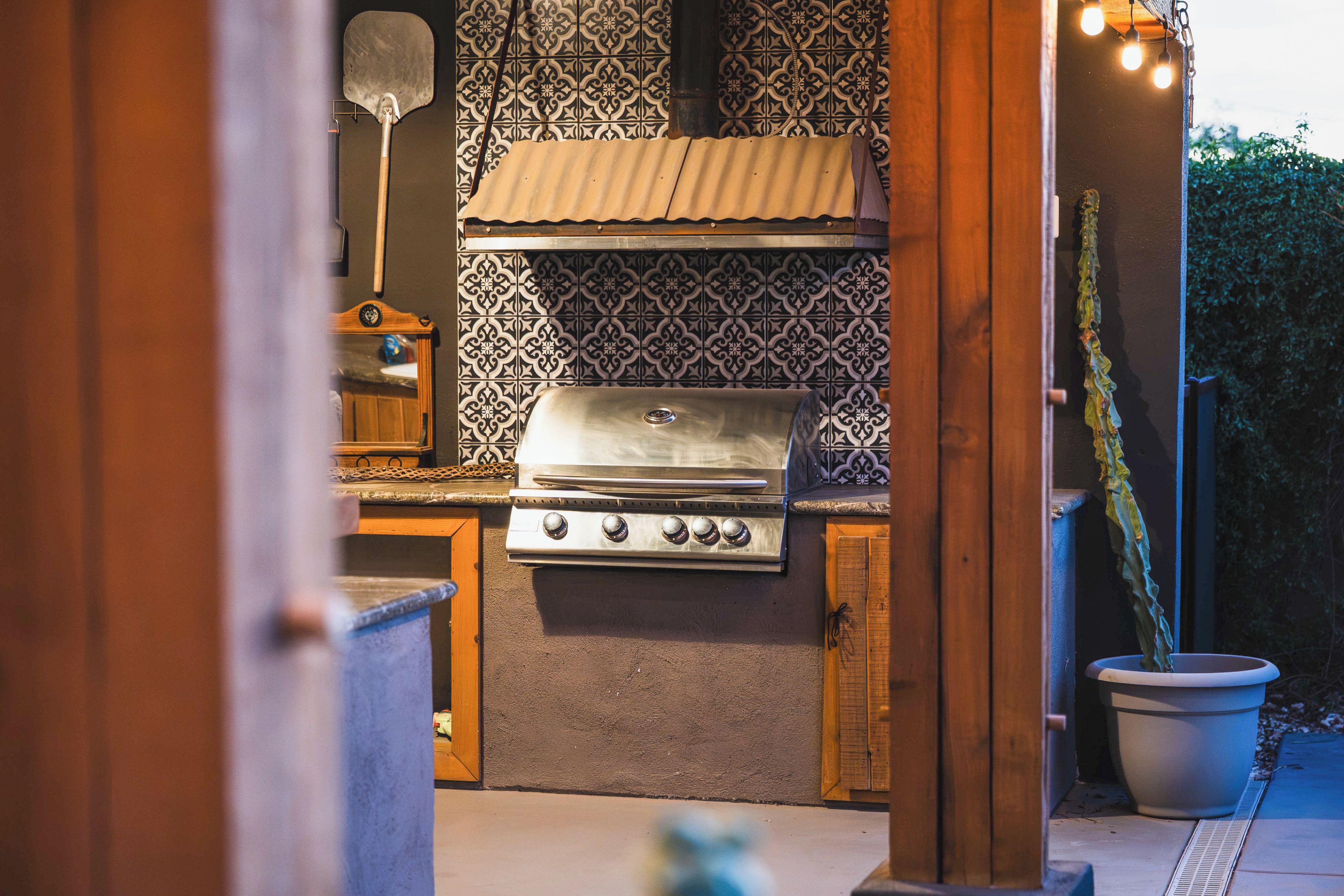 An outdoor kitchen with a grill, a wooden cabinet, and patterned tiles.