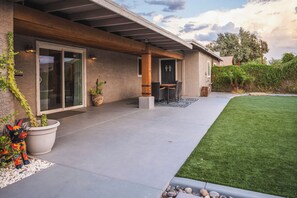A modern house with a covered patio, a lawn, and a garden with plants and a decorative sculpture. - 11327 Desert Oasis w/ Year-Round Pool (Apache Junction)