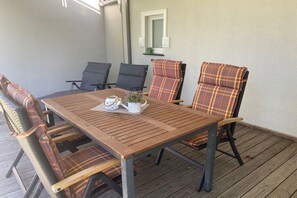 Eine Holzterrasse mit Tisch und Stühlen, einem Blumentopf und einem an der Wand befestigten Regal.