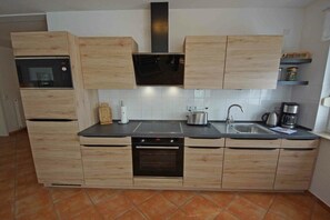 Eine moderne Küche mit Holzschränken, einem eingebauten Ofen, einer Mikrowelle und einem Edelstahl-Spülbecken.