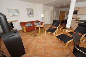 Een woonkamer met een bank, stoelen, een televisie en een open haard.