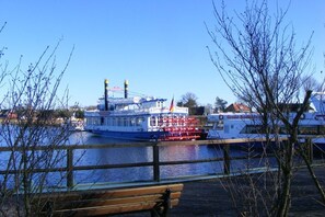 A riverfront with a large boat docked, a wooden bench, and leafless trees. - Holiday apartment with 3 bedrooms (Ostseebad Prerow)