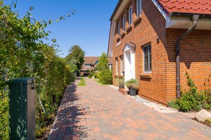 Eine Wohnstraße mit Backsteinhäusern, einem gepflasterten Gehweg und viel Grün.