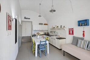 A compact kitchen with white cabinets, a dining table with chairs, and a sofa in a living area. - A Casa di Anna (Naples)