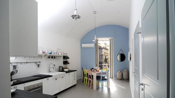 Une cuisine avec des meubles blancs, un plan de travail noir et un coin repas agrémenté de chaises colorées.