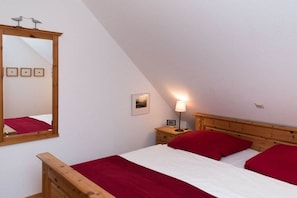 Ein Schlafzimmer mit schrägem Dach, einem Bettgestell aus Holz, einem Nachttisch mit Lampe und einem Spiegel.