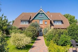Ein zweistöckiges Haus mit Ziegelaußenwand, einem zentralen Eingang und einem Gartenweg, der zur Haustür führt.