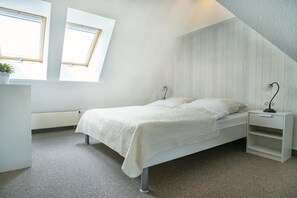 A bedroom with a sloped ceiling, a bed with a white bedspread, a nightstand with a lamp, and a window with a view. - Enjoy the cozy Klaas vacation apartment at Trollhüs in Norddorf on Amrum (Norddorf auf Amrum)