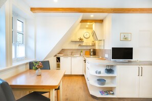 Una cocina moderna con armarios blancos, una mesa de comedor con sillas, un televisor y un reloj en la pared.