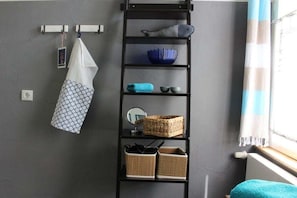 Ein Zimmer mit einem schwarzen Metallregal an einer grauen Wand, das verschiedene Gegenstände wie eine blaue Schale, einen gewebten Korb und ein gefaltetes Handtuch beherbergt.