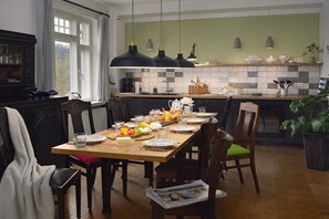 Een eetgedeelte met een houten tafel, gedekt voor een maaltijd, stoelen en een raam met gordijnen.