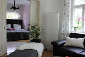 Een slaapkamer met een bed, een potplant, een zwarte leren bank en een raam met gordijnen.
