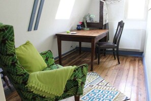 Ein Zimmer mit einem grün gemusterten Sofa, einem Holztisch mit einem Stuhl, einem gemusterten Teppich und einem Fenster mit Vorhängen.