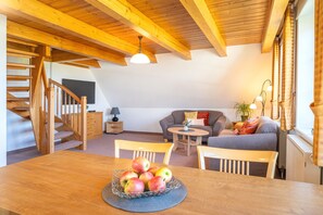 Un intérieur en bois avec un escalier, un canapé, une table à manger avec des pommes et une lampe.