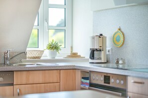Eine Küche mit Kaffeemaschine, Blumentopf und Fenster.