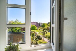 Ein Fenster mit mehreren Scheiben, durch die man einen Blick auf eine Wohngegend mit Häusern und viel Grün erhaschen kann.