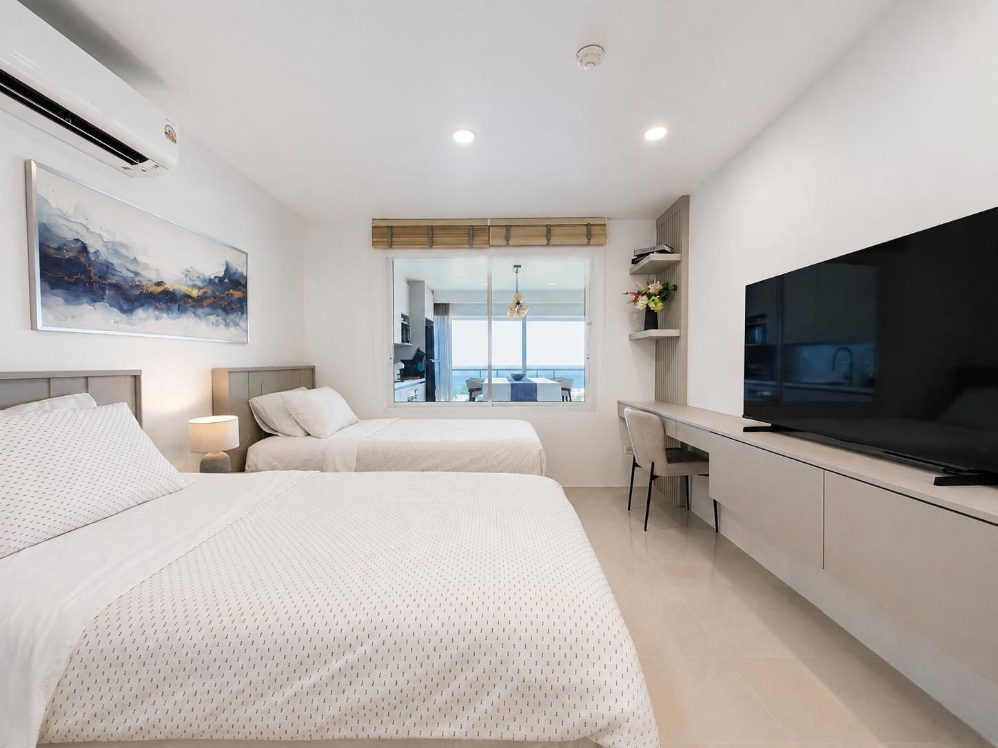 Una habitación de hotel moderna con dos camas, un escritorio, un televisor y un amplio ventanal con vistas.