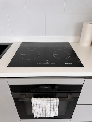 Una cocina con una placa de inducción negra, un horno empotrado y una toalla colgada del mango del horno.