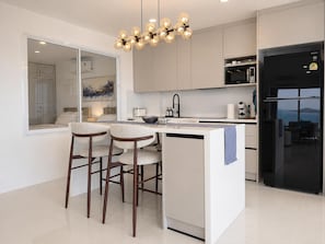 Una cocina moderna con una isla central, taburetes de bar, un refrigerador negro y vista al mar.