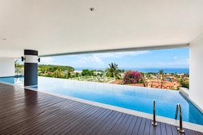 Ein Pool ohne Ende mit Blick auf das Meer und einer Holzterrasse.