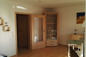 Um quarto com porta de madeira, um armário com portas de vidro, uma mesinha e uma cadeira.