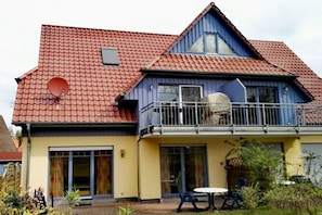 Ein zweistöckiges Haus mit rotem Ziegeldach, einem Balkon mit Geländer und einer Satellitenschüssel.