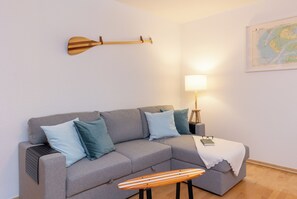 Ett modernt vardagsrum med en grå soffa, blå kuddar, en träpanel som hänger på väggen, ett litet träbord, en lampa och en karta på väggen.