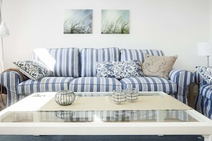 A striped sofa with patterned cushions, a glass coffee table with decorative items, and two abstract wall art pieces. - in the heart of the old town (Heiligenhafen)