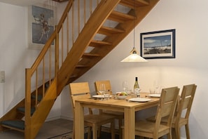Ein Essbereich mit einem Holztisch, gedeckt für vier Personen, einer Holztreppe und einer Pendelleuchte.
