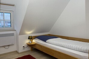 A small, single-bed room with a sloped ceiling, a window, a bedside lamp, and a red rug. - Holiday apartment with 2 bedrooms (Büsumer Deichhausen)