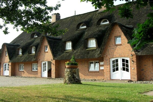 Eine Reihe traditioneller Backsteinhäuser mit Strohdächern und weiß gefassten Fenstern.