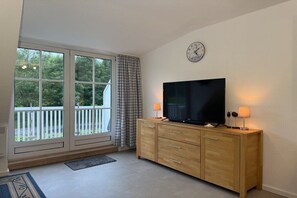 Ein Zimmer mit großem Fenster, einem Flachbildfernseher auf einem Holzkasten und einer Wanduhr.