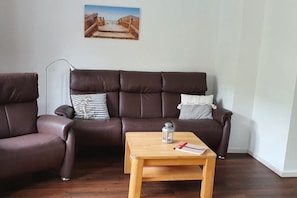 A brown leather sofa with striped and white pillows, a wooden coffee table with a lantern and a book, and a framed picture on the wall. - Holiday home with 3 bedrooms (St.Peter-Ording)