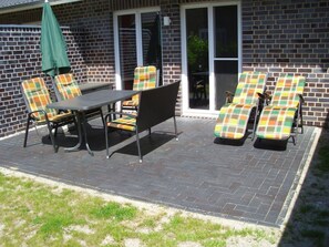 An outdoor patio with a table and chairs, a green umbrella, and a brick wall. - Holiday home with 3 bedrooms (St.Peter-Ording)