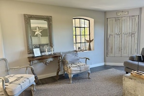 A room with a vintage chair, a mirror, a small table with decorative items, and a window with a view. - Holiday home with 2 bedrooms (Steinberg)