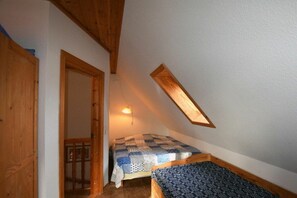 Una habitación pequeña y acogedora con techo inclinado, una cama individual con colcha estampada y una lámpara fijada a la pared.